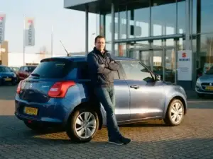 Zelfverzekerde klant leunend tegen een glanzende Suzuki Swift op het voorterrein van een dealer in warm middagzonlicht.