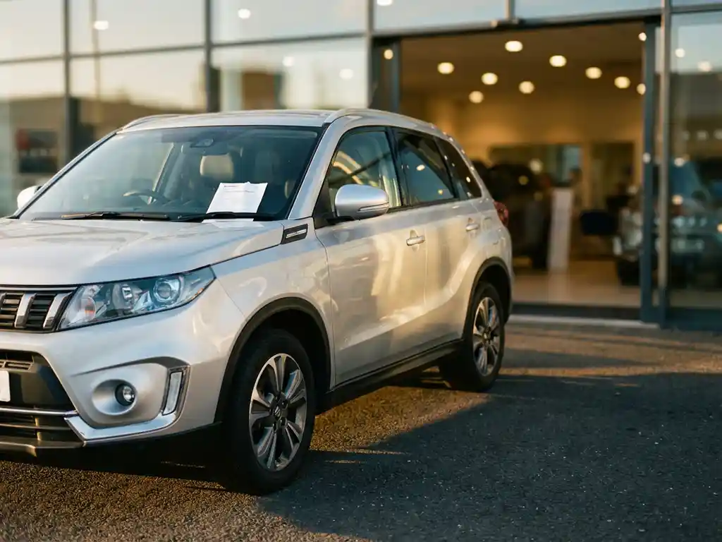 Zilveren tweedehands Suzuki Vitara op het voorterrein van een autodealer met een leasedocument achter de voorruit.