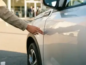 Hand die de deurpaneelnaad inspecteert van een zilveren Suzuki Swift op een zonnig dealerterrein.